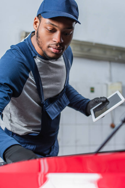 afro-amerikai technikus egyenruhában tartja digitális tabletta üres képernyő közelében elmosódott autó - Fotó, kép