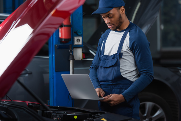 young african american technician using laptop near car with open hood - Photo, image
