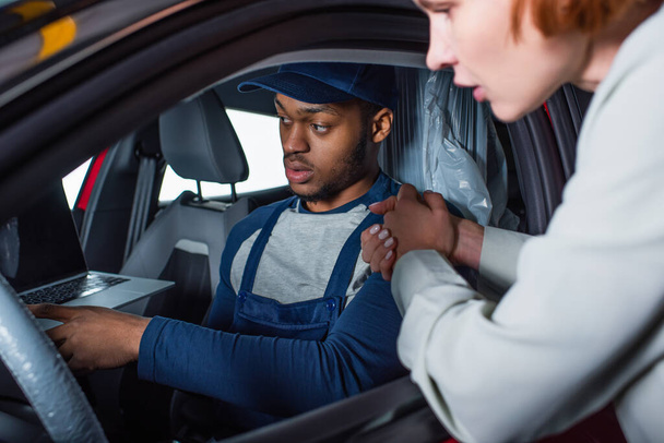 african american foreman pointing at laptop while sitting in car of blurred client - Фото, изображение