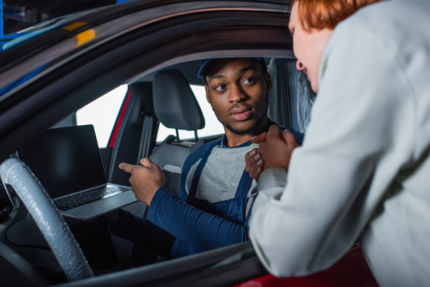 african american technician pointing at laptop while sitting in car near blurred customer - Photo, Image