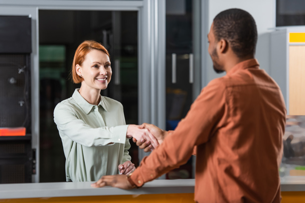 smiling car dealer shaking hands with blurred african american customer  - Foto, Bild