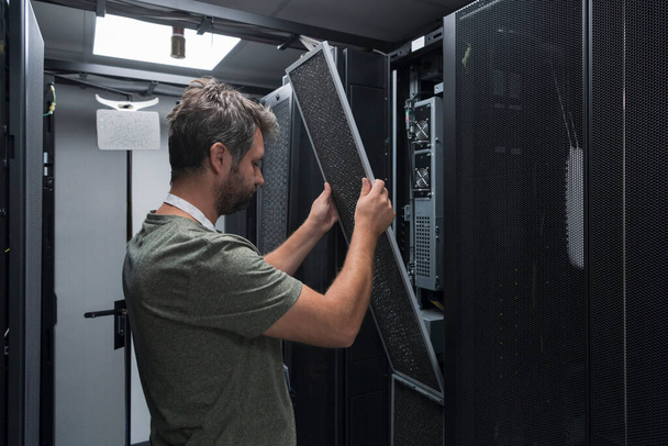 IT engineer working In the server room or data center. The technician puts in a rack a new server of corporate business mainframe supercomputer or cryptocurrency mining farm.  - Φωτογραφία, εικόνα