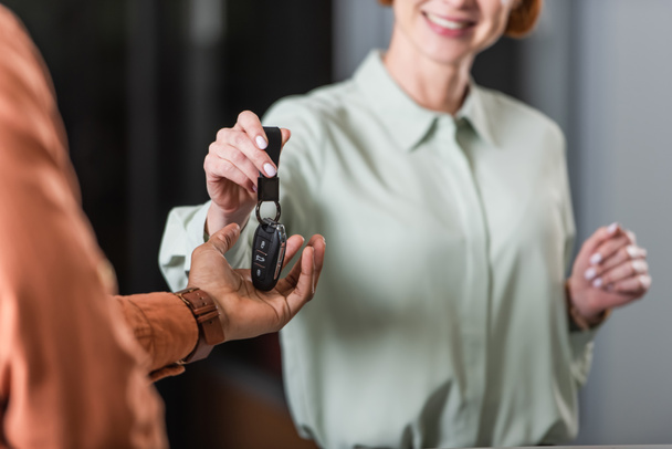 cropped view of smiling car dealer giving key to blurred african american man - Φωτογραφία, εικόνα