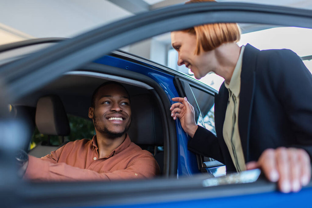 happy african american man sitting in car near blurred car dealer - Foto, Imagen