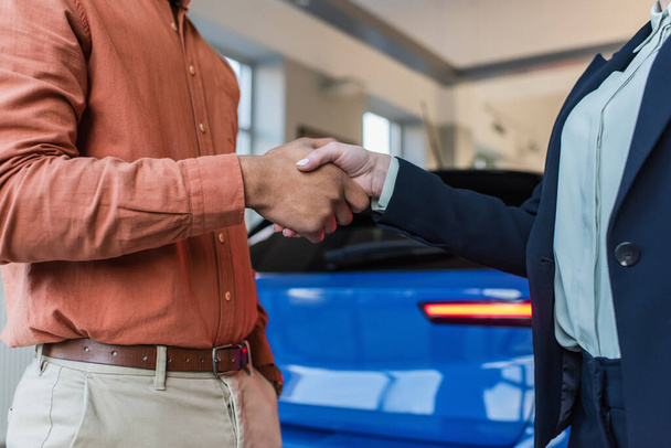 Araba satıcısının ve Afrikalı Amerikalı müşterinin galeride bulanık arabanın yanında el sıkışması. - Fotoğraf, Görsel