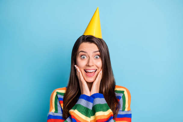 Photo portrait of amazed girl overjoyed wearing yellow headwear on birthday touching cheeks isolated on bright blue color background - 写真・画像