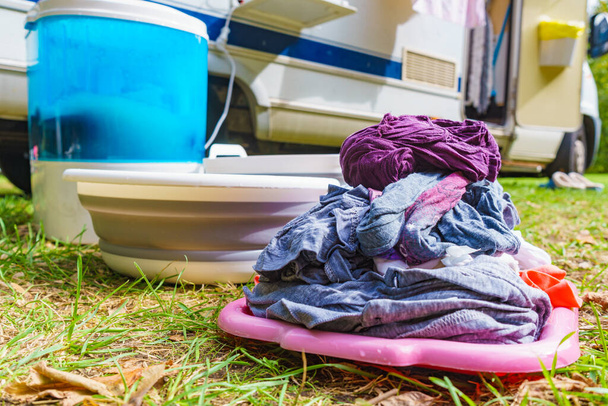 Doing laundry outdoor at caravan. Bowl with clean clothes and washing machine working. Camping on campground - Photo, image