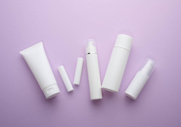 fles en lege witte plastic buizen voor cosmetica op een paarse achtergrond. Verpakking voor crème, gel, serum, reclame en product promotie, mock up - Foto, afbeelding