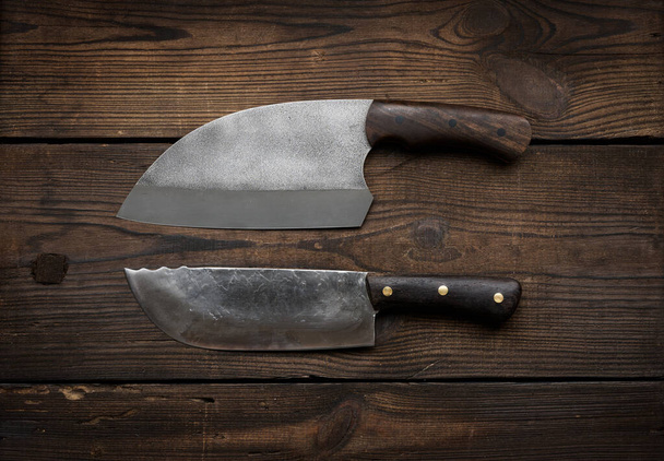 metal sharp kitchen knives in a wooden handle on a brown table made of boards, top view - Foto, Imagem