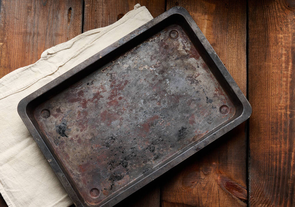 lege rechthoekige ijzeren roestige bakplaat op een houten bruine tafel, bovenaanzicht - Foto, afbeelding
