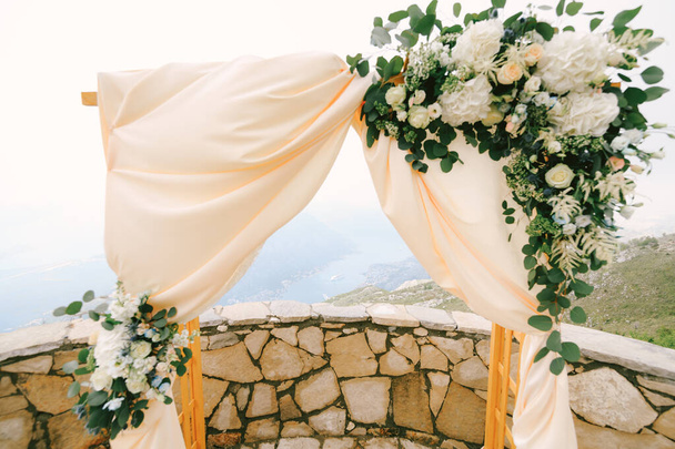 Wooden rectangular wedding arch decorated with satin, flowers and green leaves - 写真・画像