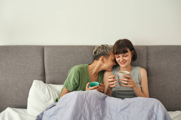 Young lesbian couple rest and drink tea on bed - Valokuva, kuva