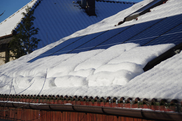 Zonnepanelen bedekt met sneeuw. Fotovoltaïsche elektriciteitsinstallatie op het dak tijdens het winterseizoen op een zonnige dag. PV-energieproductie. Lage prestaties en efficiëntie bij koud weer. - Foto, afbeelding