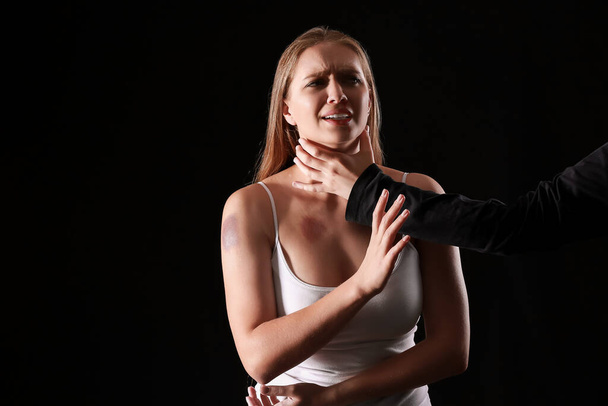 Hombre sosteniendo a mujer asustada por el cuello sobre fondo oscuro. Concepto de violencia - Foto, imagen