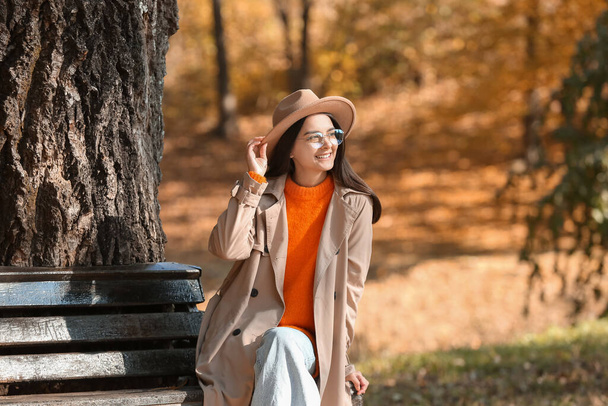 Parkta güneşli bir günde bankta oturan modaya uyan genç bir kadın. - Fotoğraf, Görsel