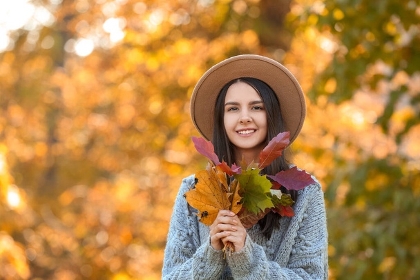 Beautiful fashionable woman with bouquet of different leaves in autumn park - 写真・画像