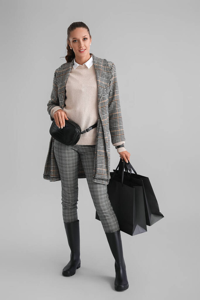 Elegantní žena s nákupními taškami na šedém pozadí - Fotografie, Obrázek