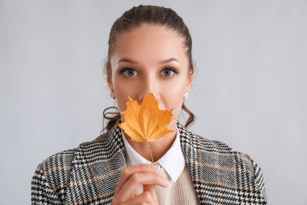 Gri arka planda sonbahar yaprağıyla ağzını kapatan güzel bir kadının portresi. - Fotoğraf, Görsel