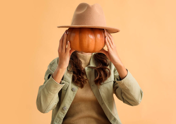 Woman holding pumpkin with felt hat on color background - Фото, изображение