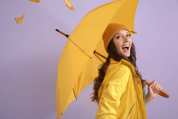 Femme heureuse en imperméable avec parapluie ouvert sur fond de couleur - Photo, image