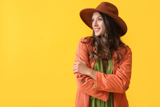 Portrét krásné usmívající se ženy ve stylovém podzimním oblečení na žlutém pozadí - Fotografie, Obrázek