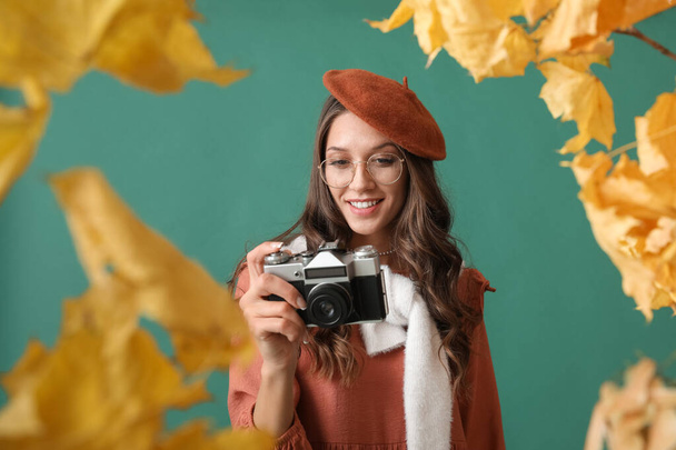 Belle femme parisienne utilisant un appareil photo vintage dans un cadre fait de feuilles d'automne sur fond vert - Photo, image