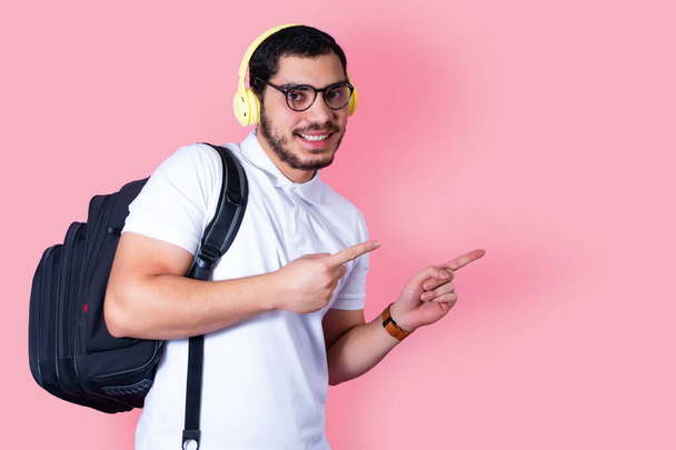 Young student with backpack, points with on fingers, smiles on a pink background. - Zdjęcie, obraz