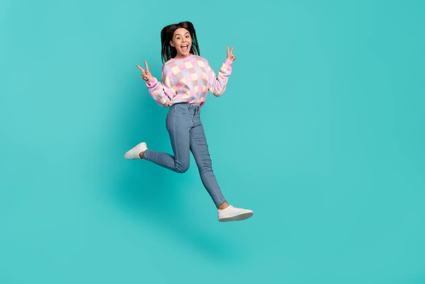 Full length body size view of charming cheery girl jumping showing v-sign isolated over bright teal turquoise color background - Foto, afbeelding