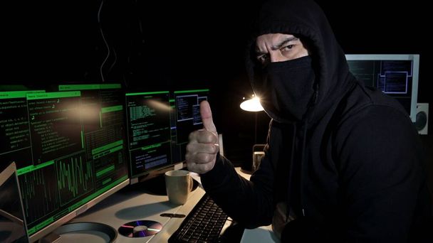 Cyber hacker with hood and covered face looks at the camera showing thumb up with hand. Cyber attack. - Foto, immagini
