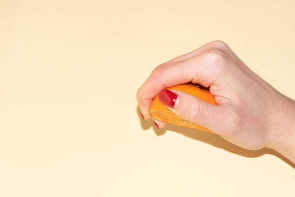 close-up shot of female hand with squishing orange half on light color background - Фото, изображение