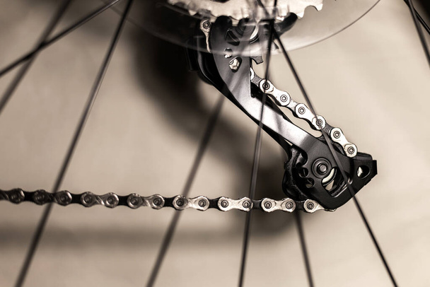 Part of a new bike on a light background, rear derailleur mechanism and chain through the spokes from the wheel, close-up - Foto, Bild