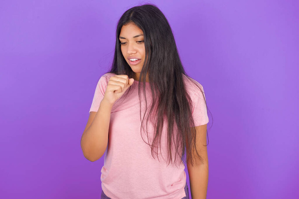 Chica morena hispana con camiseta rosa sobre fondo morado sintiéndose mal y tosiendo como síntoma de resfriado o bronquitis. Concepto sanitario. - Foto, Imagen