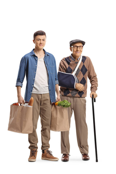 Young man helping an elderly man with a broken arm and carrying grocery shopping bags isolated on white background - Foto, immagini