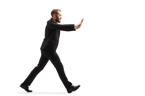 Full length profile shot of a businessman walking and pushing with hands isolated on white background - Photo, image