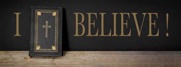 I BELIEVE - Church faith Christian background banner panorama - Old holy bible with golden cross on old rustic vintage wooden table and black wall - Foto, immagini