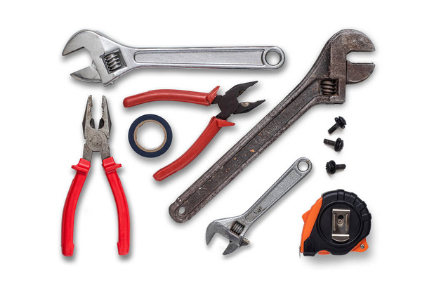 Several wrenches, pliers, measuring tape measure, unscrewed bolts and insulating tape on a white background - Photo, image