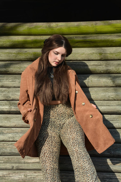 Une jeune femme avec un manteau marron, posant devant de vieilles planches de bois - Photo, image