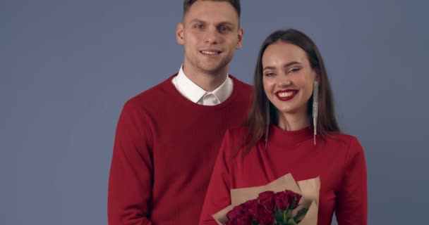 Feliz pareja joven con ramo de rosas rojas sobre fondo gris. Celebración de San Valentín - Metraje, vídeo