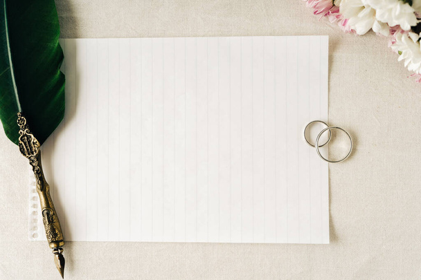 Algunos anillos de boda o de compromiso junto con un viejo lápiz y papel para escribir una nota. Hermosas flores acompañan la composición. Concepto de amor, espacio de copia. - Foto, Imagen