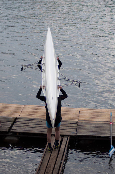 Mužský závodní tým nese veslařský člun a umístí ho na vodní hladinu. - Fotografie, Obrázek