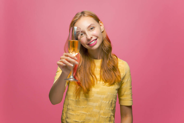 Beautiful happy female celebrating holiday holding glass of champagne, smiling, congratulating on pink studio background - Valokuva, kuva