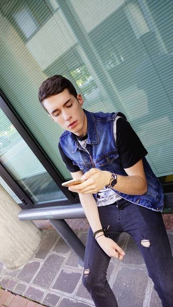 Красивый мальчик в джинсовой куртке использует смартфон, фото высокого качества - Фото, изображение