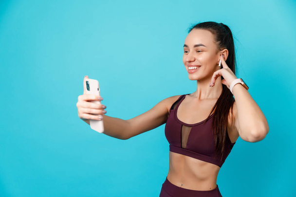 Young Slim Lady Wearing Wireless Earphones, Favorite Song, Playlist For Training, Isolated Over blue Studio Background - Foto, Bild