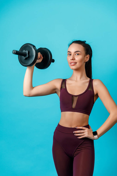 beautiful sportive brunette girl holding dumbbells on a blue background. charger. isolated - 写真・画像