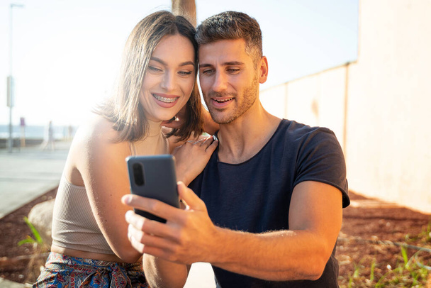 Νεαρό ευτυχισμένο ζευγάρι βγάζει selfie με κινητό τηλέφωνο ή μιλάει online με φίλους, χαμογελώντας στο smartphone. Καλοκαίρι. Διακοπές. Ταξιδιώτη. Πραγματικός τρόπος ζωής. - Φωτογραφία, εικόνα