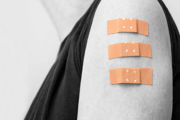 Human arm with three medical plasters after vaccinations against covid-19, initial immunization, repeat and third booster dose, color key - black and white effect, copy space, selected focus, narrow depth of field - Photo, image