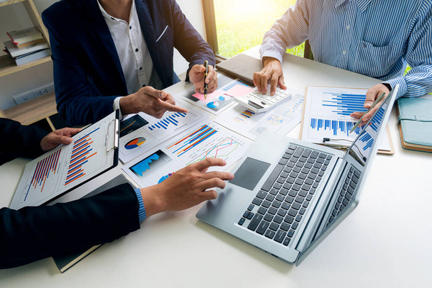 Collaborate at office desks to discuss paperwork. A financial group of business people is meeting to analyze data for a marketing plan on a table with graphs and a laptop with a calculator. - Foto, Imagem