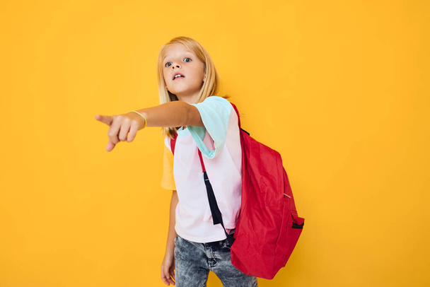 小さな女の子ブロンドの髪学校のバックパックポーズ黄色の色の背景 - 写真・画像