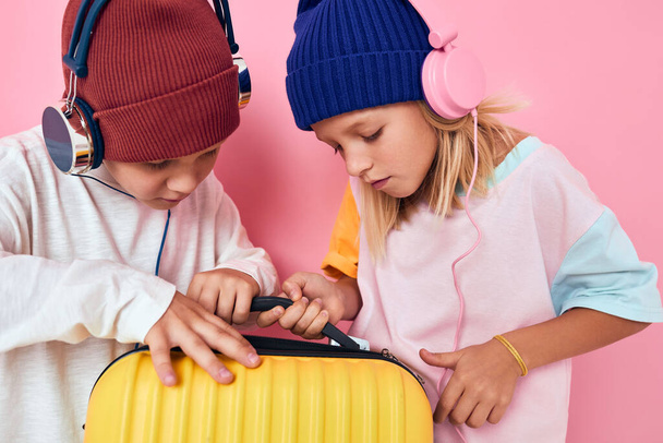 iloinen poika ja tyttö tyylikäs vaatteet matkalaukku kuulokkeet vaaleanpunainen väri tausta - Valokuva, kuva