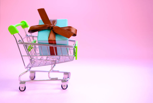 Een geschenkdoos met een lint in een winkelwagentje. Concept - een geschenk kopen, online en verkoop. - Foto, afbeelding